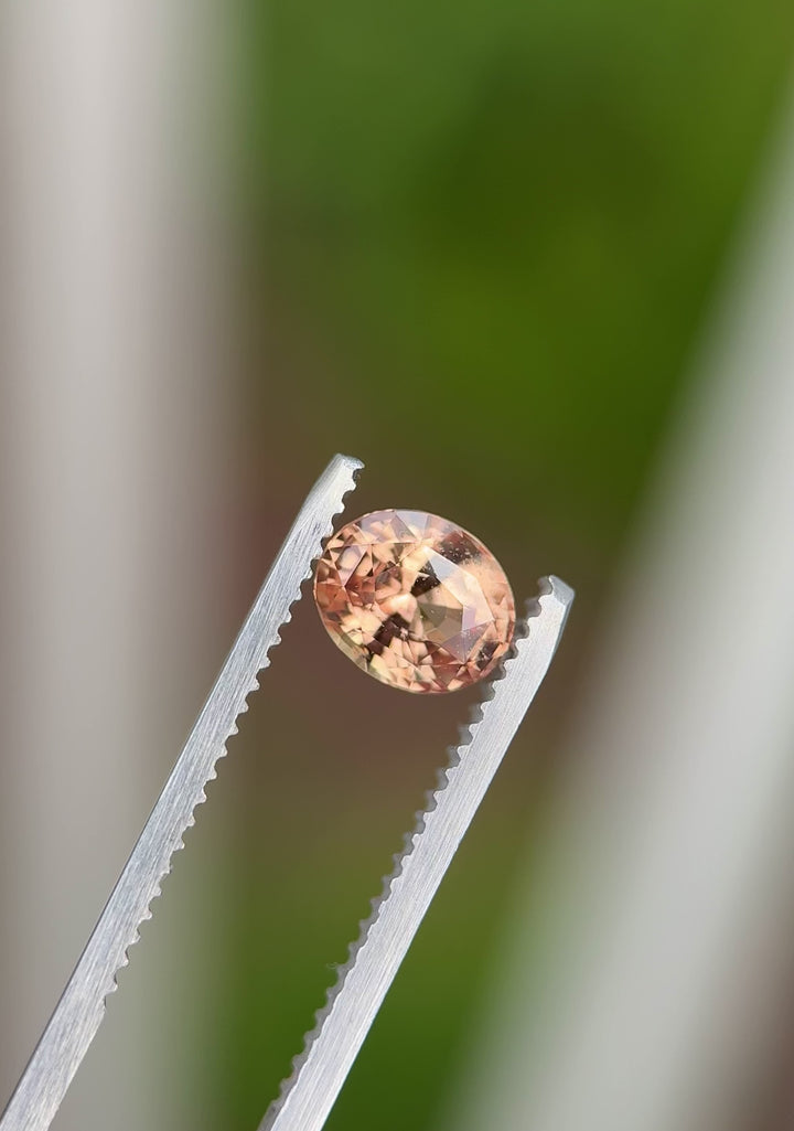 360-degree video of 1.51ct untreated oval sapphire in peach, orange, and pink, captured in tweezers under direct lighting