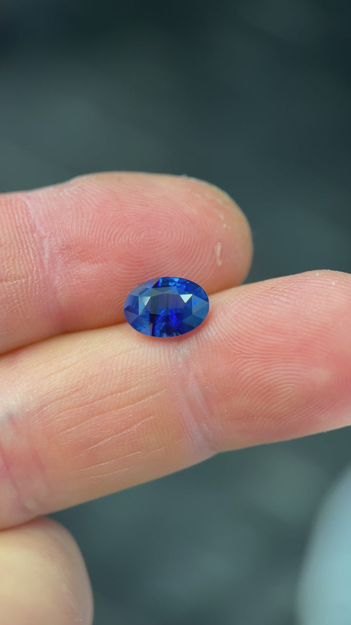 Close-up video showing a 2.56-carat royal blue parti sapphire in motion, highlighting striated blue zoning, sparkle, and precision oval mixed cut details while held in gemstone tweezers, untreated.