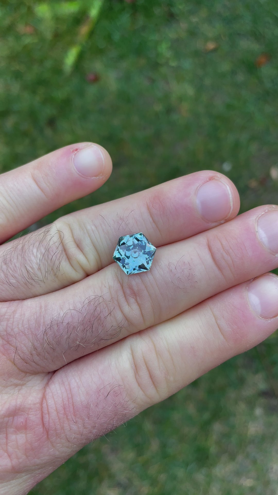 Outdoor video presenting a 5.79-carat hexagonal modified brilliant sapphire in a natural setting, highlighting how sunlight plays off its surfaces to reveal the depth of its green and blue colors.