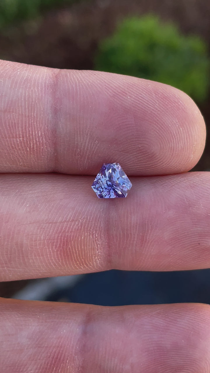Close-up video of a 1.56-carat lavender sapphire, cut in a custom mix brilliant triangle shape. This Sri Lankan-origin gemstone displays mesmerizing brilliance, with hues of lavender, purple, and pink, making it an exceptional choice for fine jewelry