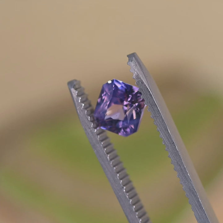Loose precision radiant cut sapphire turning in tweezers, revealing shifting violet and pink tones from Sakaraha, Madagascar.