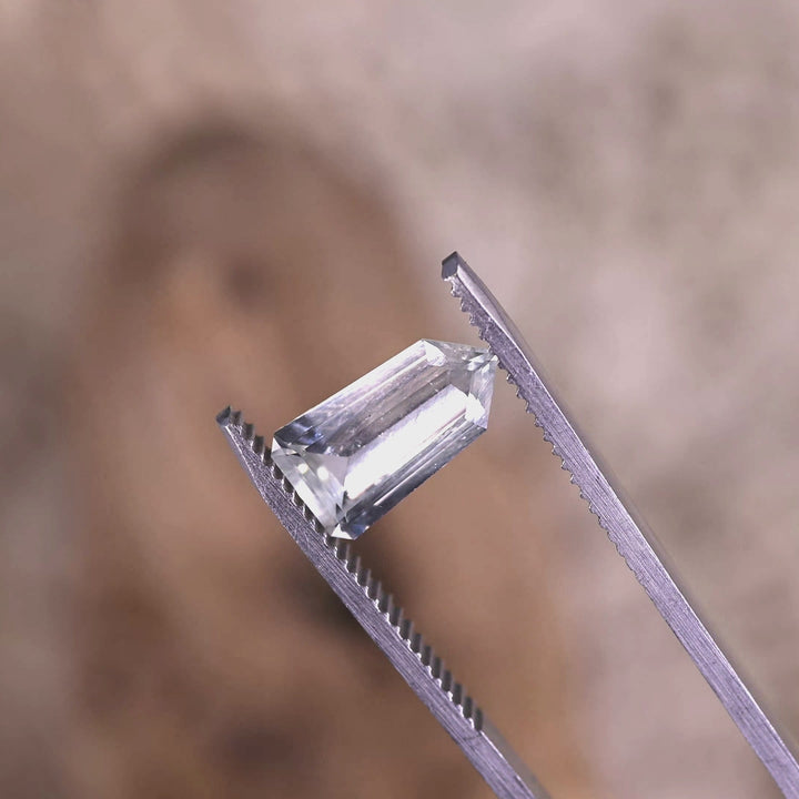 Rotating loose light seafoam no-heat sapphire from Sri Lanka in tweezers, revealing the sharp step-cut facet structure and subtle blue-green tone change as it turns under bright light.