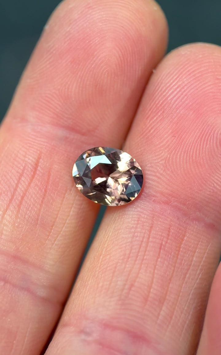 3.04 carat Madagascar sapphire pumpkin spice autumn color shift oval precision cut gemstone shown in hand for scale macro video