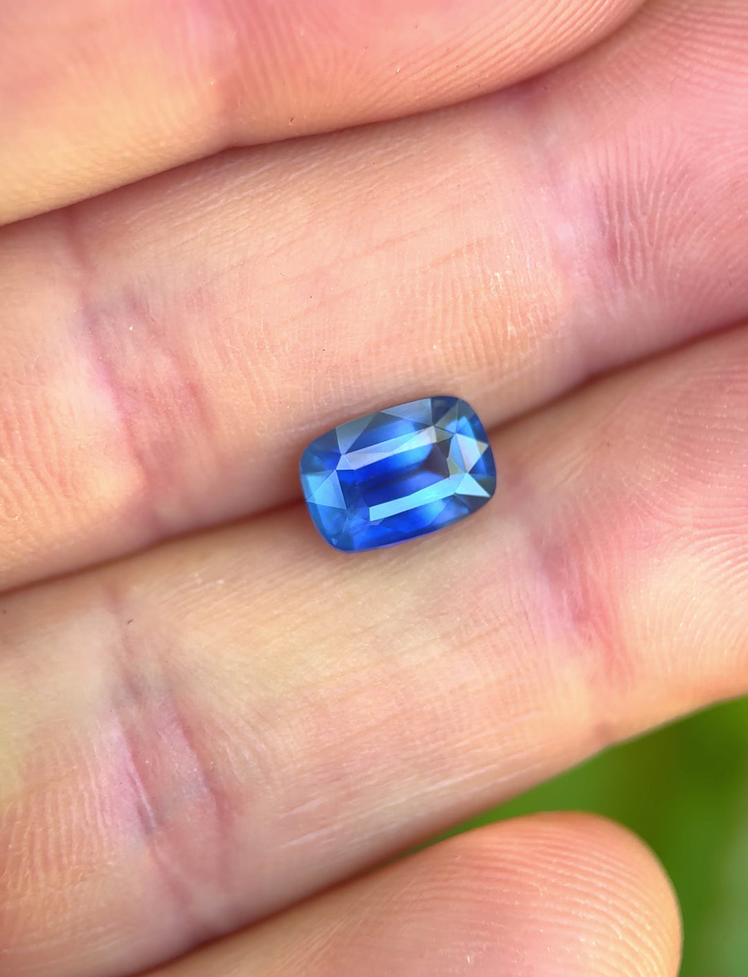 2.53ct opalescent cornflower royal blue sapphire rotating in hand, revealing shifting blue saturation and elongated cushion brilliance.