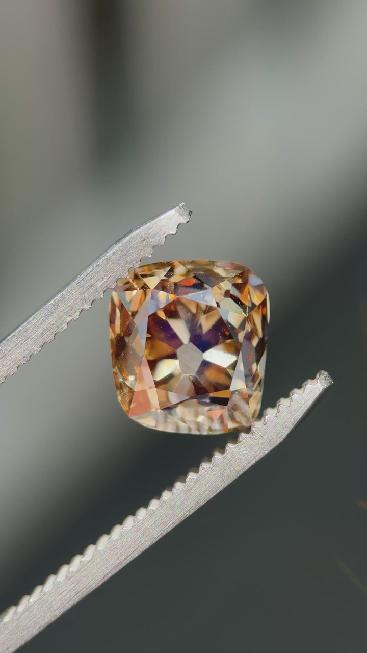 Macro video of a VVS1 Canadian champagne diamond turning in tweezers, showcasing broad vintage facets, exceptional clarity, and changing brown-gold reflections from every angle.