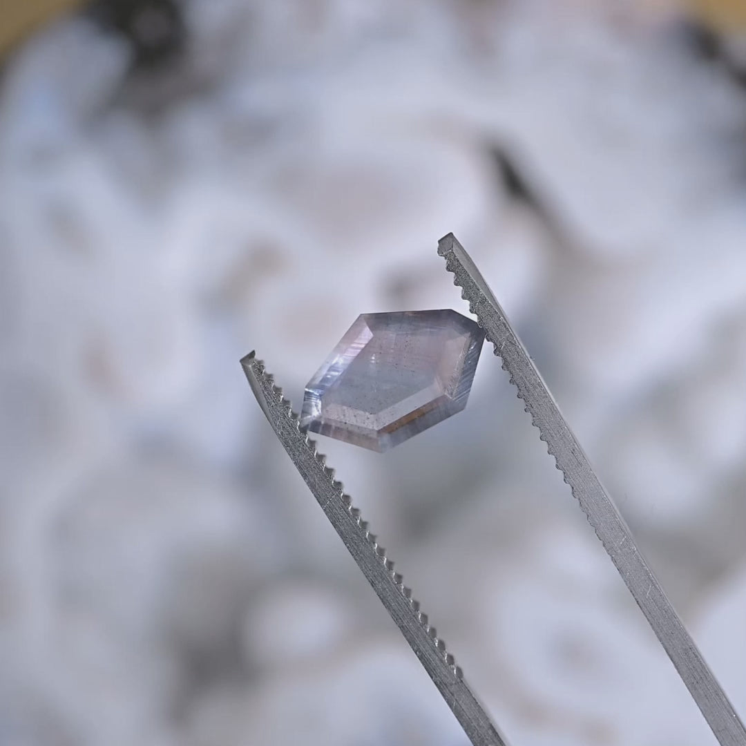 Close-up video of an untreated Sri Lanka sapphire slowly turning under light, showing purple, brown, and gray parti colors in a thin geometric portrait cut.