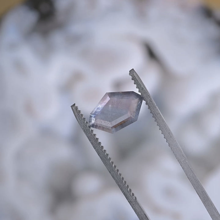 Close-up video of an untreated Sri Lanka sapphire slowly turning under light, showing purple, brown, and gray parti colors in a thin geometric portrait cut.