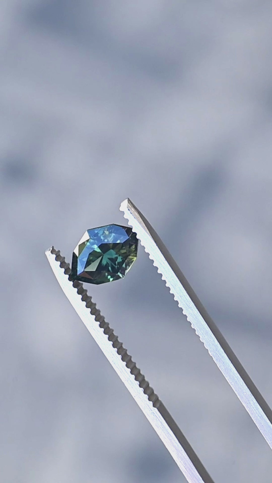 1.68ct green teal geometric marquise sapphire from Diego, Madagascar held in gem tweezers rotating under natural lighting.