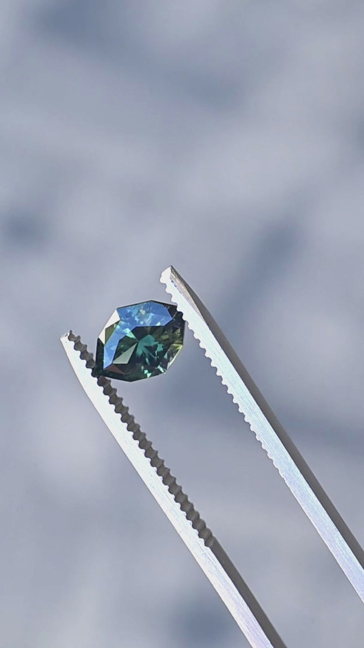 1.68ct green teal geometric marquise sapphire from Diego, Madagascar held in gem tweezers rotating under natural lighting.