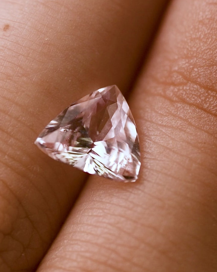 Macro video of 2.06 carat pink peach sapphire on fingertips, showing light performance, pastel hues, and facet precision of the trillion cut, unheated sapphire from Madagascar.