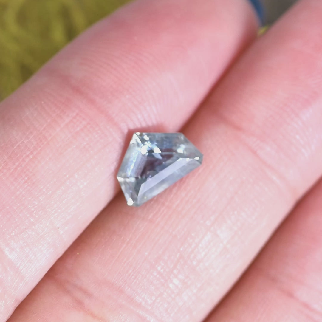Light blue Montana sapphire rotated by hand, showing the curved half moon silhouette, crisp facet reflections, and shifting icy blue tones as the stone catches the light.