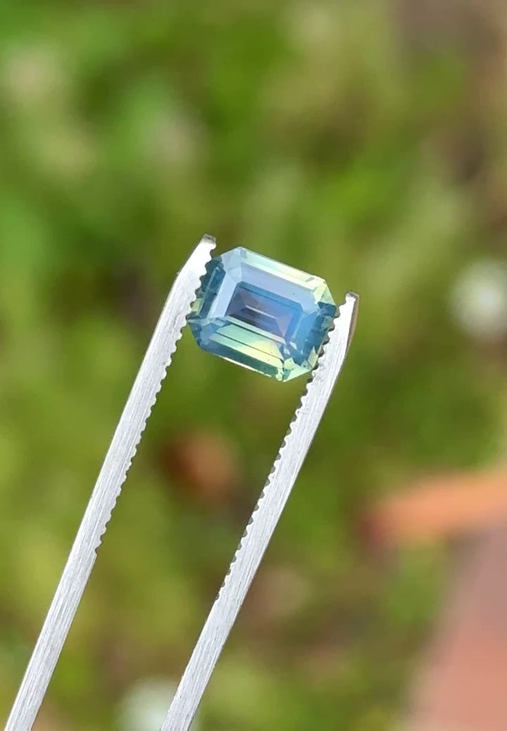 Natural Madagascar sapphire turning in tweezers, showcasing blue, green, teal, and yellow flashes under changing light.