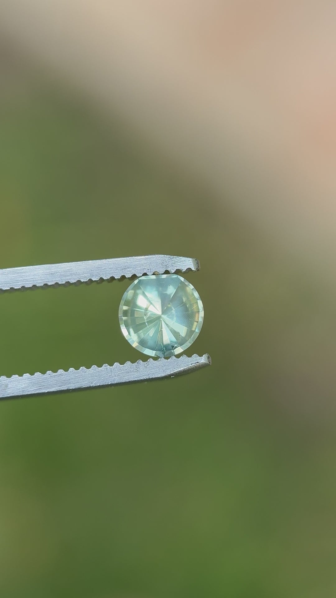 Close-up video of a 0.96-carat Malawi sapphire twirling in tweezers, capturing its radiant seafoam, teal, and yellow hues under soft daylight.
