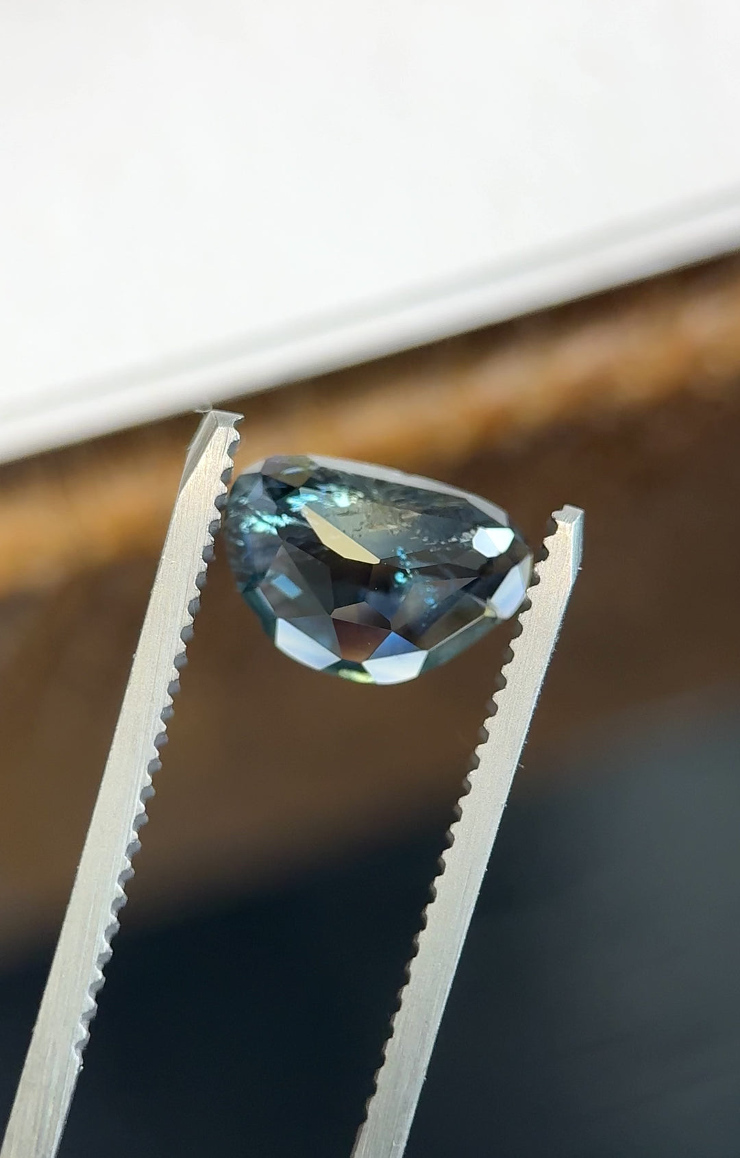 Custom trillion rose-cut sapphire turned in tweezers, displaying low-profile faceting, sharp triangular outline, and dramatic blue-to-yellow color separation.
