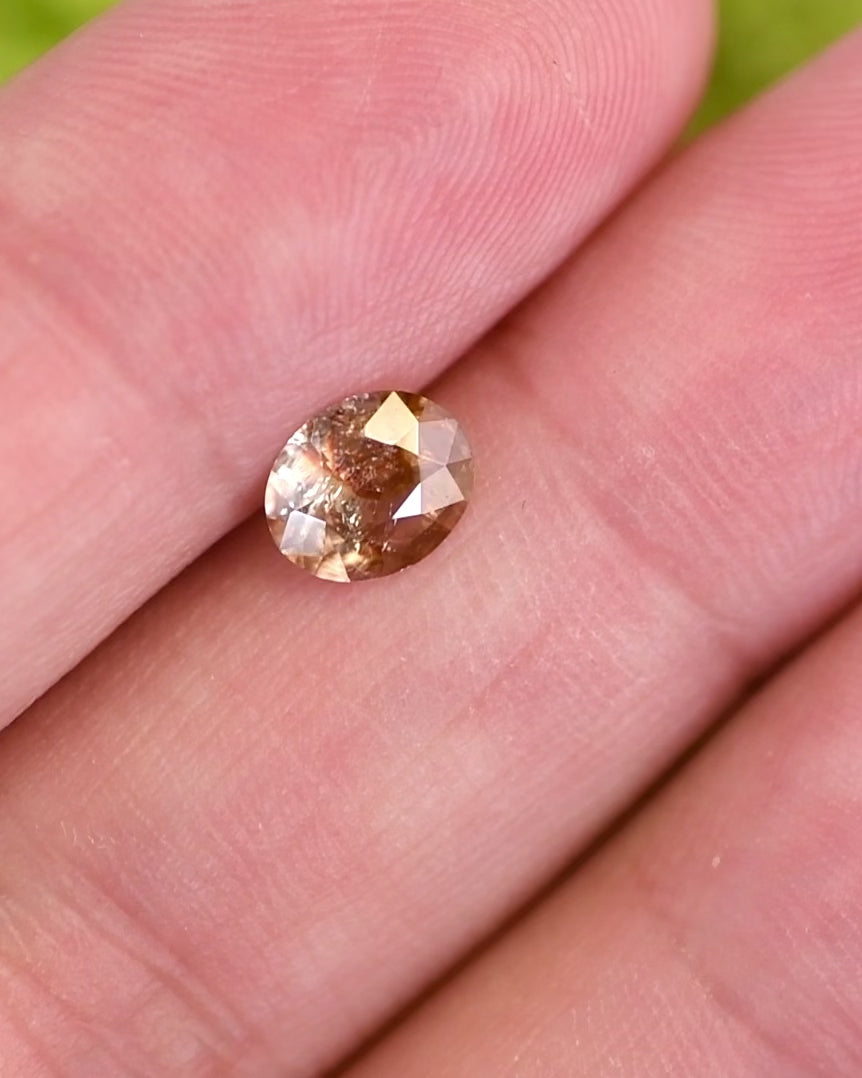 Close-up motion video of 1.05 carat orange, peach, and red sapphire rotating under natural light, displaying internal inclusions and brilliance of custom oval cut, untreated gemstone from Umba River Valley, Tanzania.