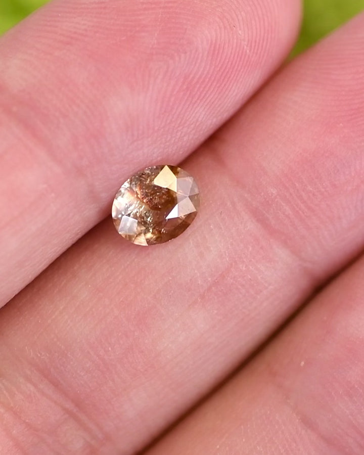 Close-up motion video of 1.05 carat orange, peach, and red sapphire rotating under natural light, displaying internal inclusions and brilliance of custom oval cut, untreated gemstone from Umba River Valley, Tanzania.