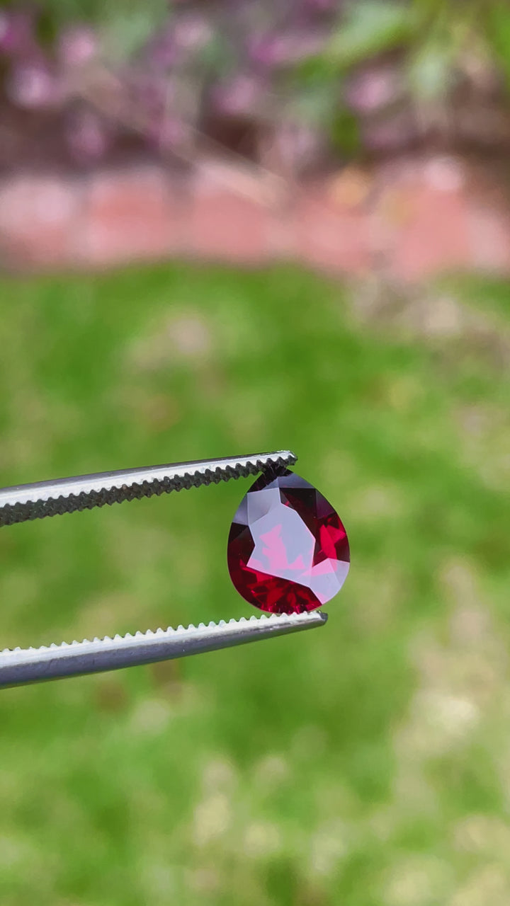 Close-up video of a pear-shaped, untreated Garnet gemstone, weighing 2.69 carats and featuring deep red to purple color transitions, sourced from Mombo, Tanzania.