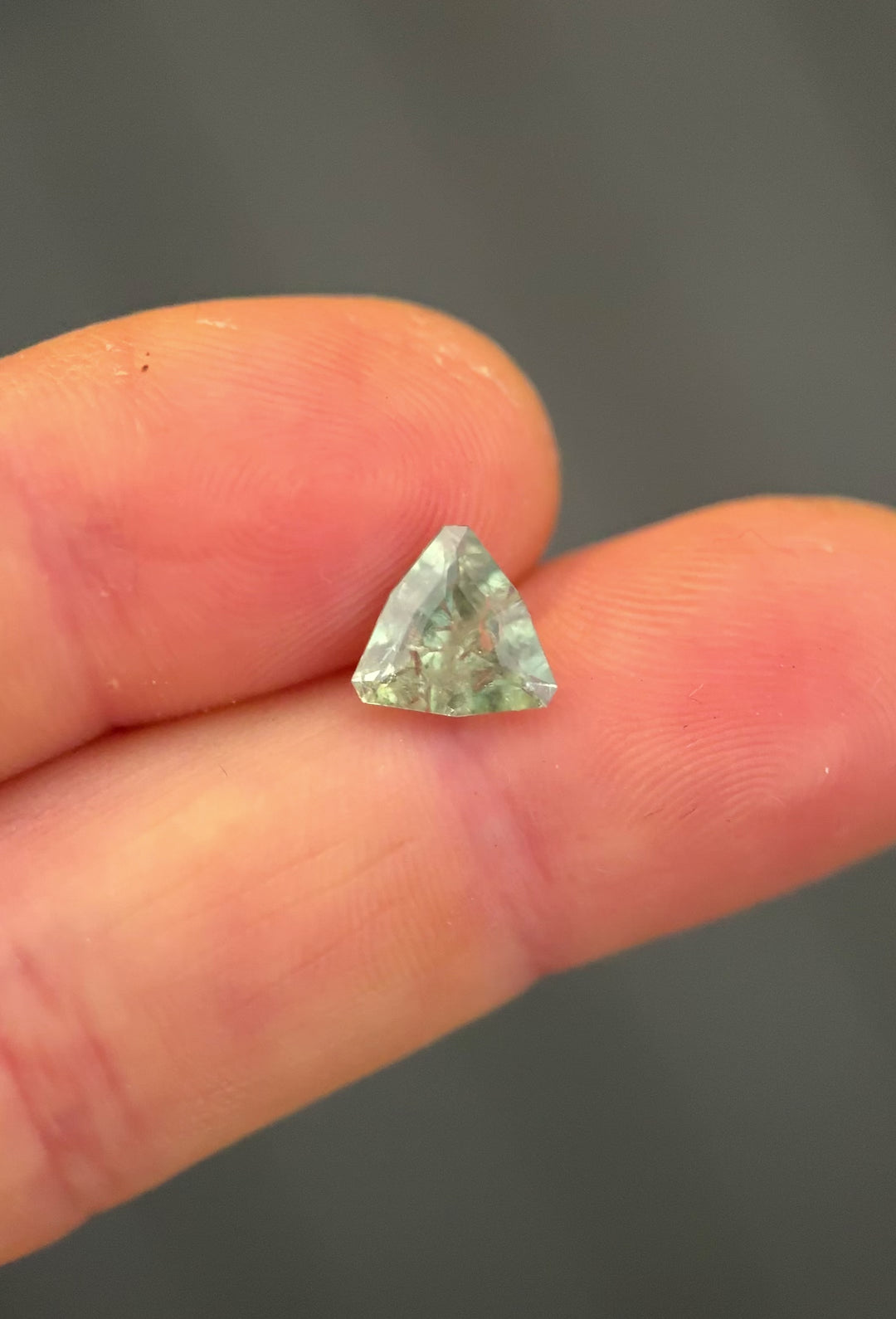 Hand-held macro video of a 2.16 carat Montana sapphire in a custom geometric trillion cut, slowly rotated to show yellow, teal, green, and sage tones and precision faceting.