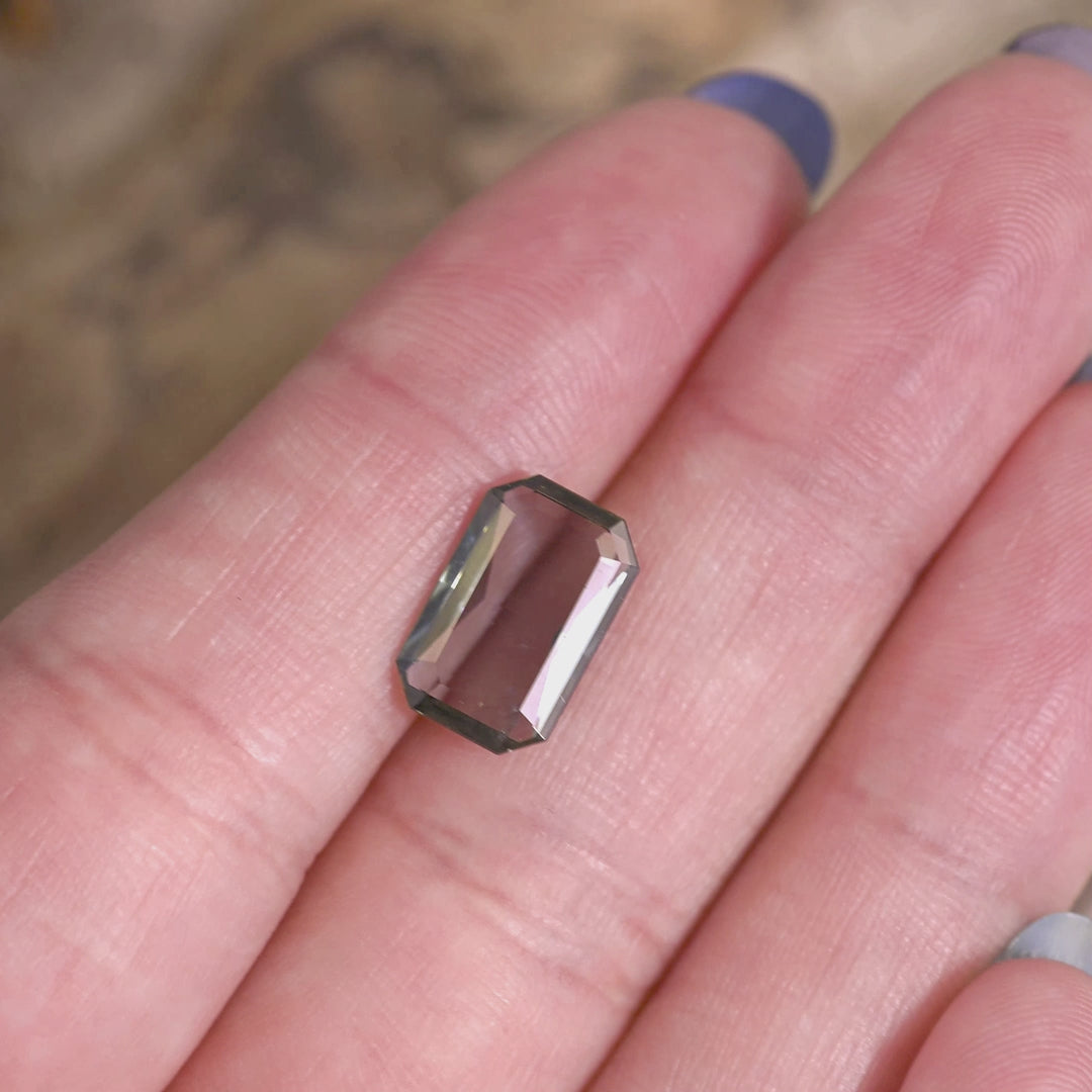 2.96 carat teal blue-green purple Tanzanite low profile emerald cut rotating on hand under natural light, Merelani Hills gemstone showing thin portrait style depth and clean step cut reflections for custom jewelry
