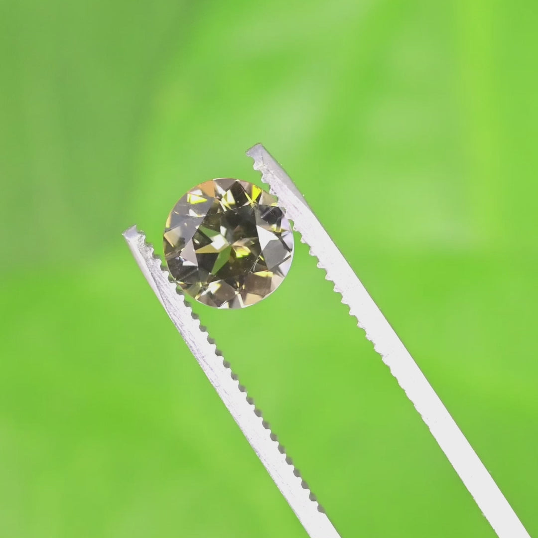 Close-up video of 1.65ct yellow orange green Tanzanite round held in tweezers, precision cut gemstone from Tanzania displaying brilliance, clarity and multicolor facet reflections