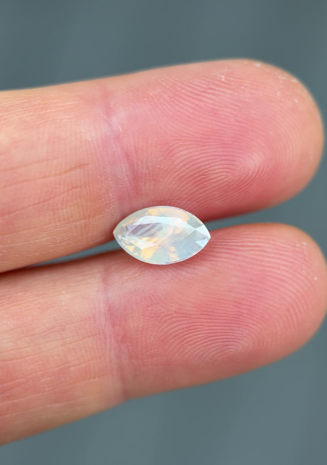 Close-up video of 2.18 carat opalescent peach and gray sapphire on fingertip in natural light, showcasing color play, facet reflections, and brilliance of the precision marquise mixed cut, untreated sapphire from Ratnapura, Sri Lanka.