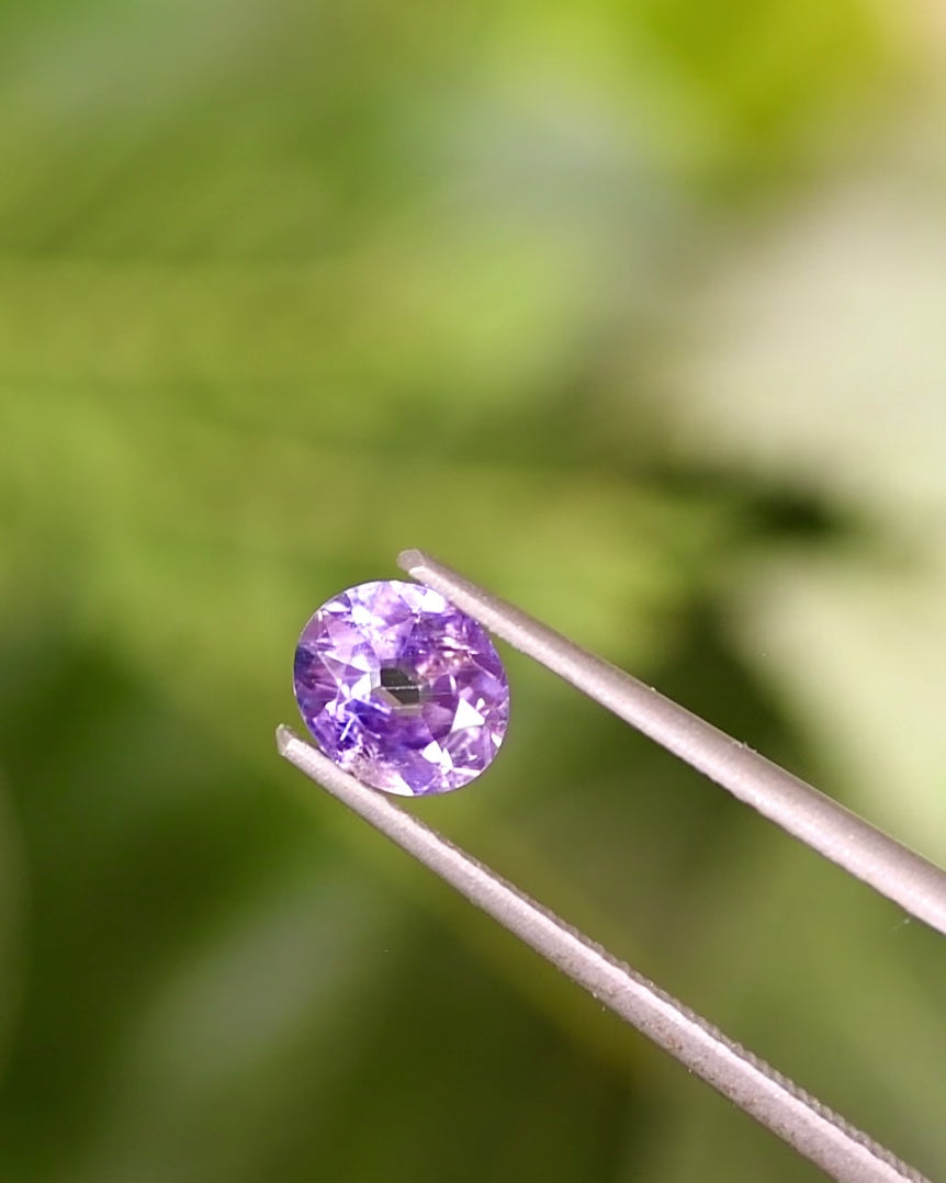 Rotation video of 0.68CT violet purple sapphire held in tweezers, showing light reflections through its modified oval cut and natural color zoning, untreated gemstone from Umba River Valley, Tanzania.