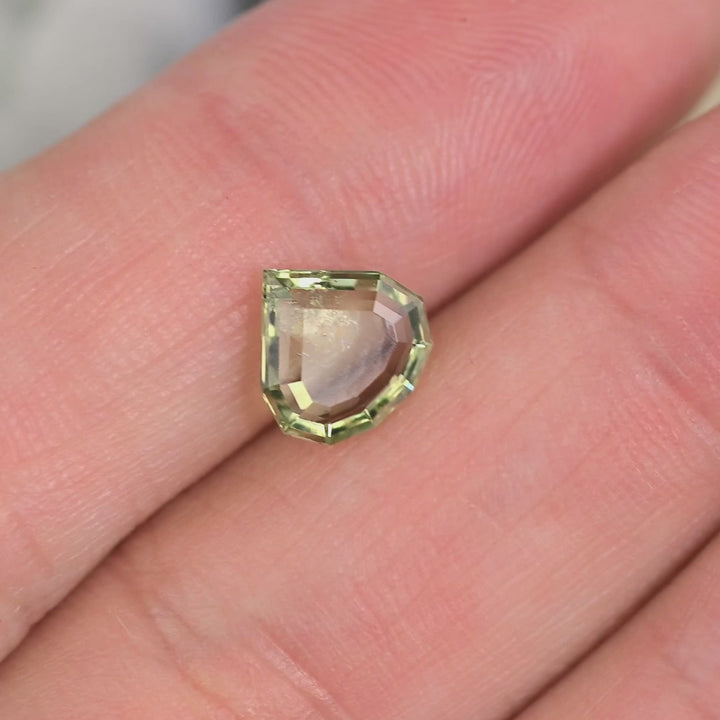 Close-up video of untreated Montana sapphire in natural light, showing color shift between teal, green, and yellow as the geometric portrait pear stone moves