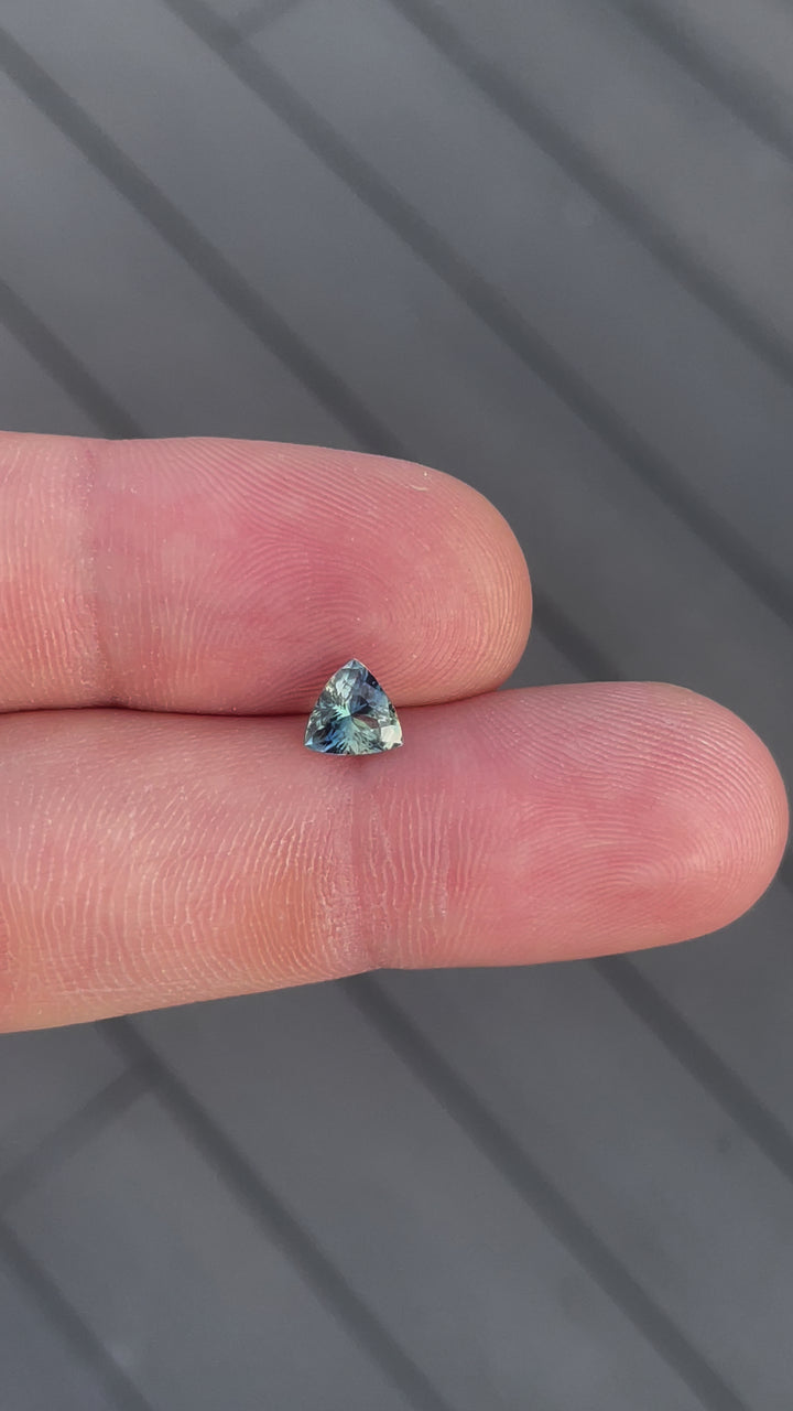 Close-up video of a 1.17-carat bi-color sapphire from Madagascar, showcasing its blue-green and yellow hues in a trillion brilliant mixed cut. This untreated gemstone sparkles under natural light, revealing its unique color transitions and clarity.