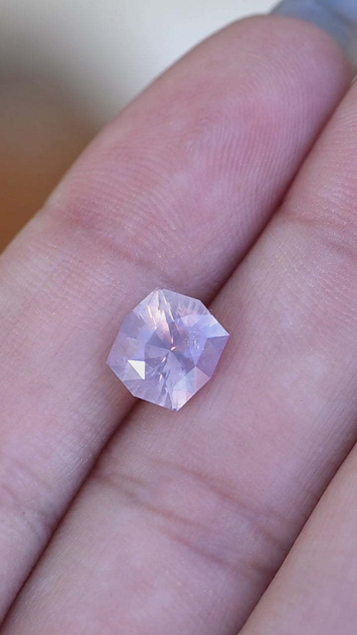 Opalescent lavender pink sapphire rotating on hand showing soft glow, lavender-pink color, and custom geometric radiant cut.