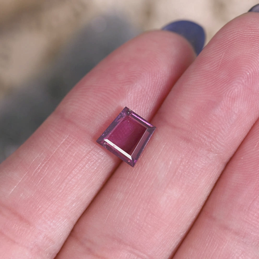 Rotating loose pink to purple garnet from Kenya shown in hand, revealing the step cut trapezoid tablet facets as the color shifts between rosy pink and plum in the light.