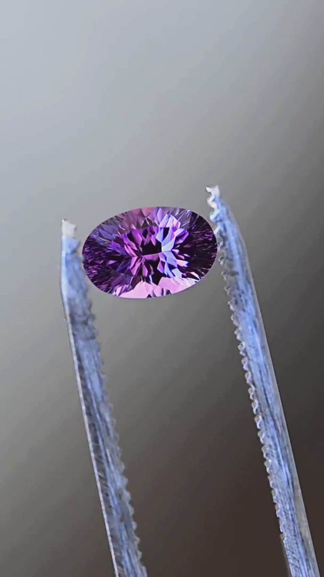 Explore the intricate faceting of this untreated 1.17ct orchid purple sapphire from Madagascar. Presented in jeweler's tweezers, the oval gemstone features lavender, violet and blue-purple reflections within its fantasy mixed-cut design.