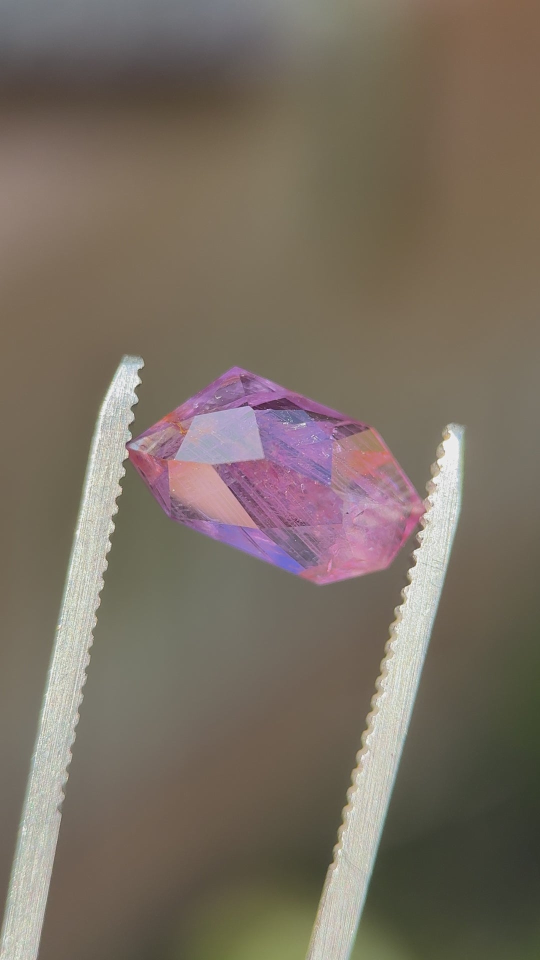 Close-up of elongated pink-purple sapphire outdoors, emphasizing internal feathering and color depth across the angled crown facets.
