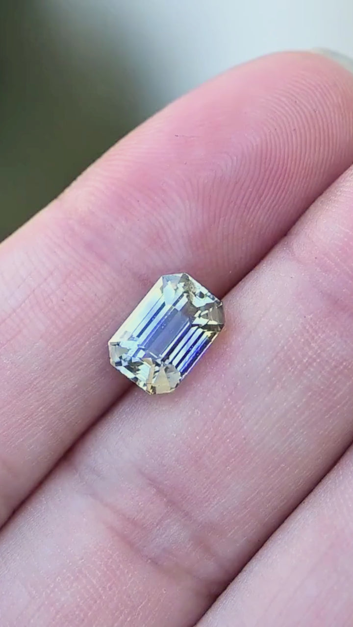 3.48 carat unheated blue and yellow parti sapphire moving on a hand, revealing shifting cornflower blue, pale yellow and near-colorless bands through its precision emerald-cut facets.