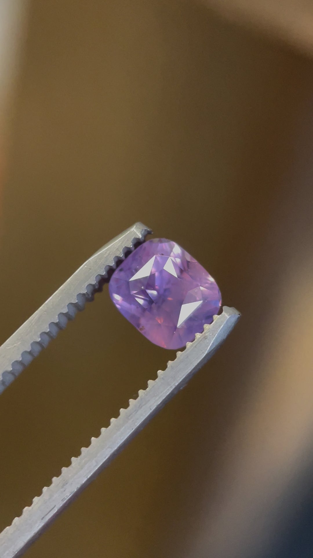 A close-up video of a 2.00-carat opalescent pink and violet sapphire, capturing its exquisite color shift and precision-cut facets as it moves in tweezers. A natural, untreated Sri Lankan gemstone.