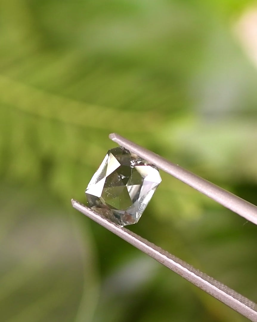 Video of 1.31CT teal yellow green sapphire turning in tweezers under natural light, showcasing its radiant sparkle and shifting hues of green and yellow, custom modified radiant cut, untreated gemstone from Umba River Valley, Tanzania.