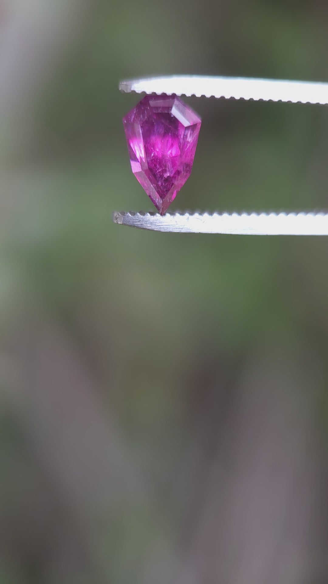 Video demonstrating the stunning features of a 2.48-carat garnet from Kenya, focusing on its custom geometric shield shape and the transition of colors from blush to red to purple, under varying light conditions.