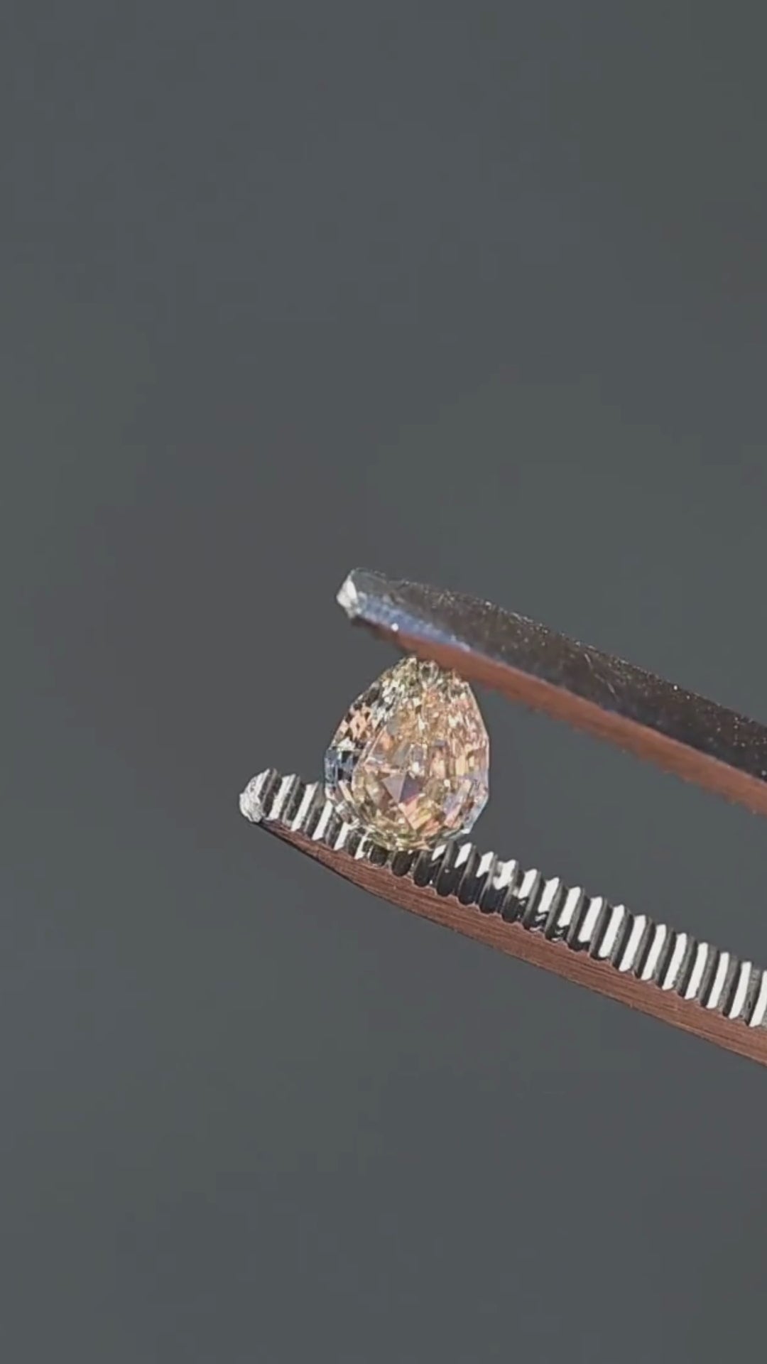Light Yellow Geo Pear step cut diamond rotating in tweezers under natural light, showcasing crisp geometric reflections, warm golden color, and natural inclusions.