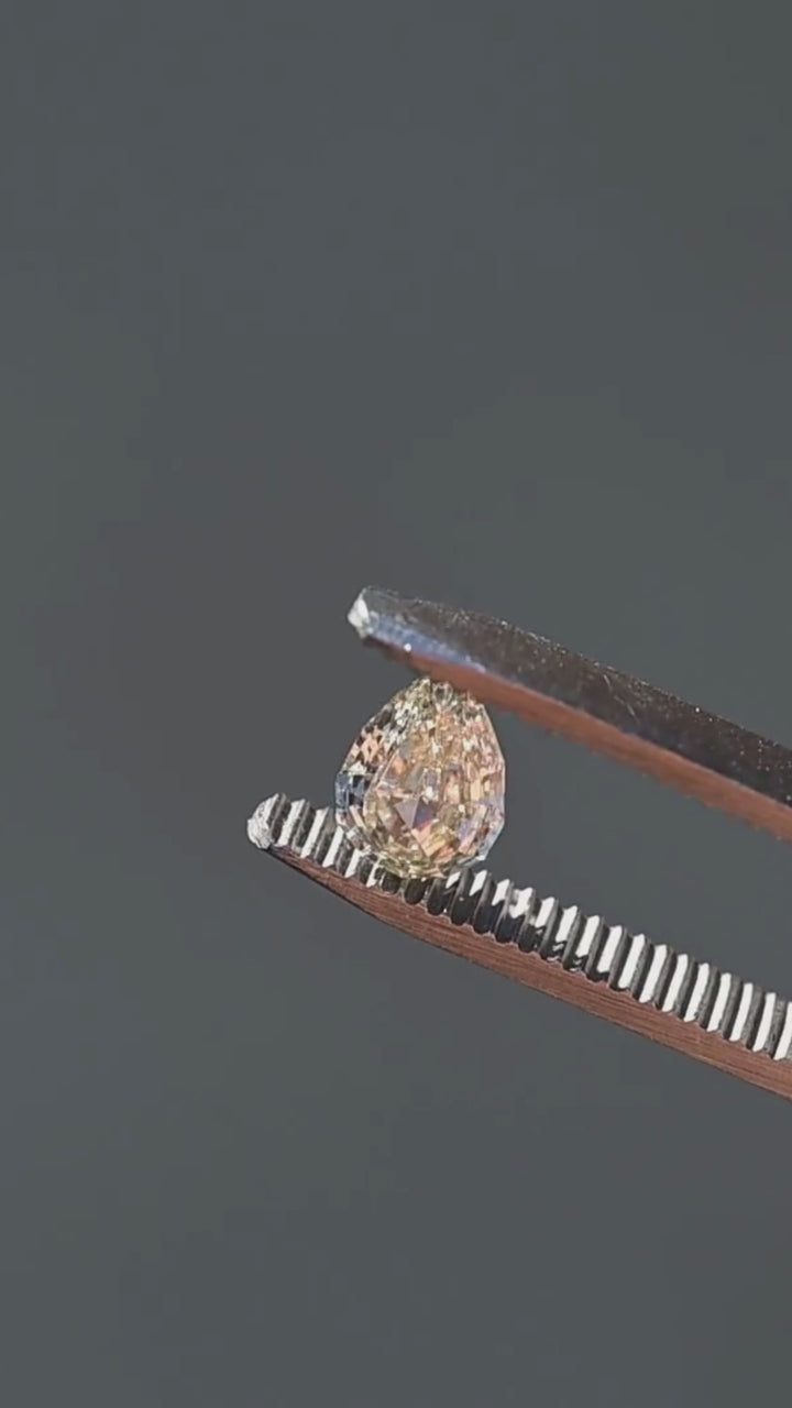 Light Yellow Geo Pear step cut diamond rotating in tweezers under natural light, showcasing crisp geometric reflections, warm golden color, and natural inclusions.