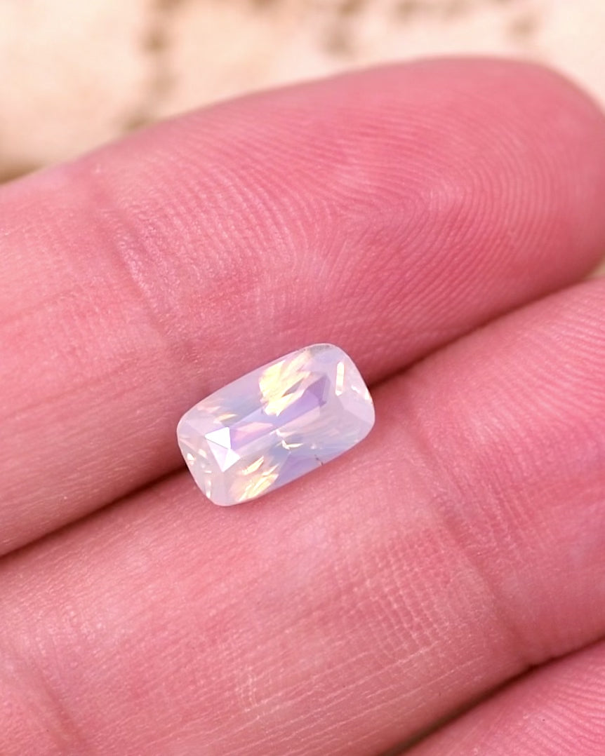 Close-up video of 2.05 carat peach opalescent sapphire resting on fingertips, showing delicate light play and faceting details of the cushion cut, unheated gemstone from Madagascar.