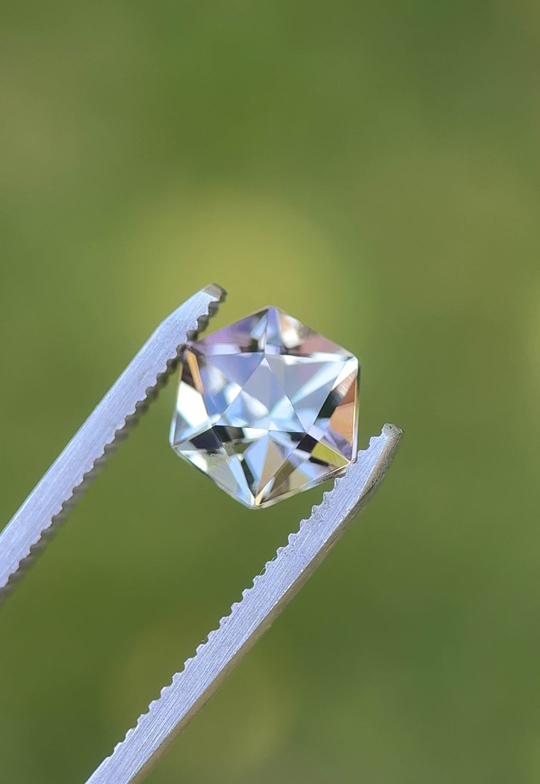 Close-up video of untreated hexagonal Tanzanite in tweezers, catching flashes of purple, green, and sky blue under outdoor lighting.