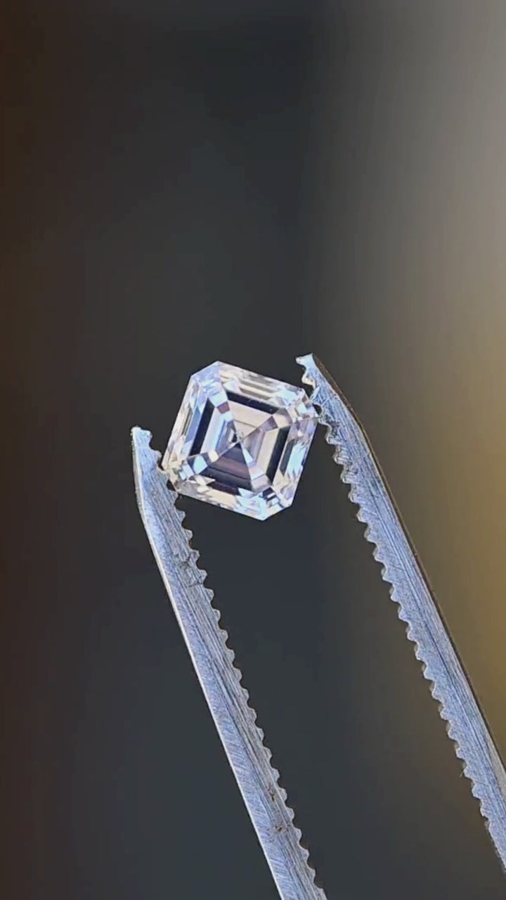 1.03 carat M VVS1 Asscher cut diamond moving in jeweler’s tweezers, revealing its clipped-corner profile, concentric steps and hall-of-mirrors light play.