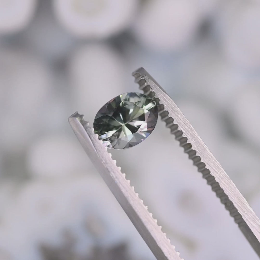 Close-up video of 1.11ct violet teal green oval Tanzanite held in tweezers, precision faceted mix modified brilliant gemstone from Tanzania displaying bright starburst reflections