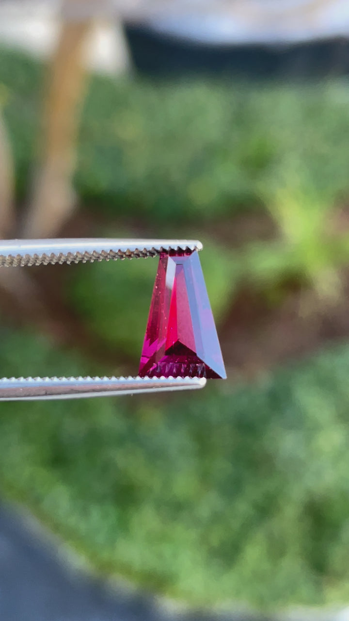 360-degree view of a tapered baguette garnet gemstone, 2.02 carats, highlighting its exquisite red and purple hues under natural light.