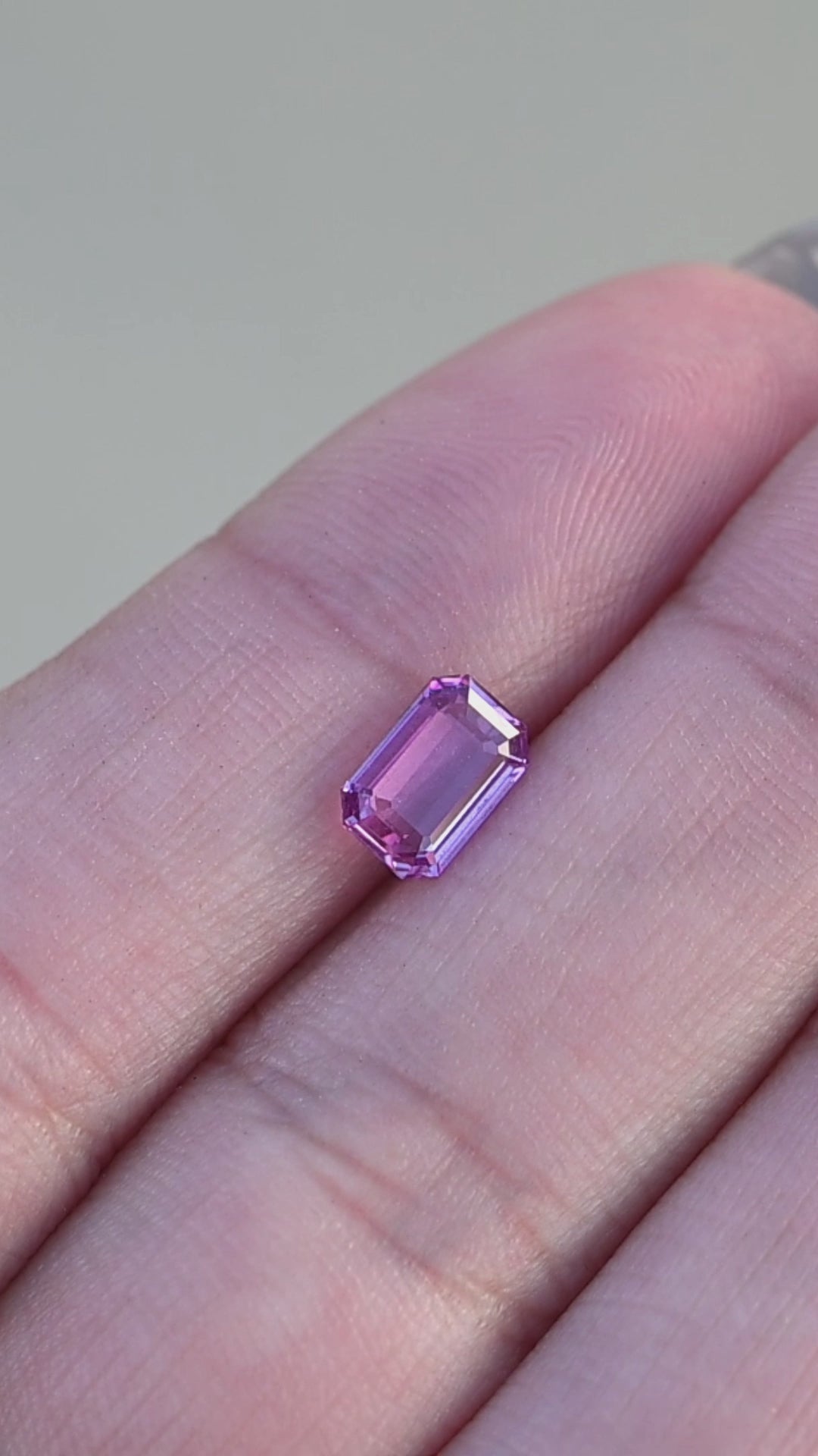Natural hot pink sapphire from madagascar held in fingertips rotating under natural light.