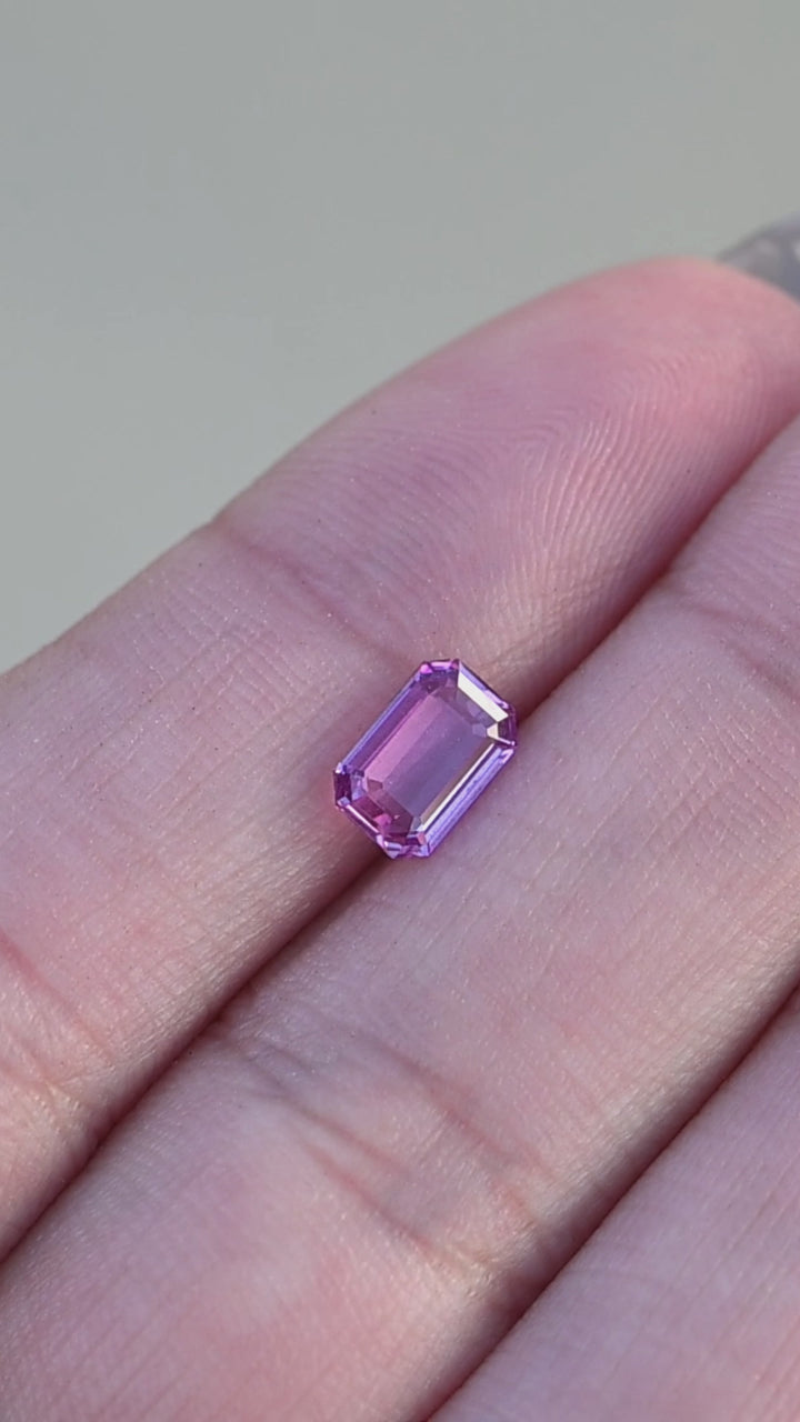 Natural hot pink sapphire from madagascar held in fingertips rotating under natural light.