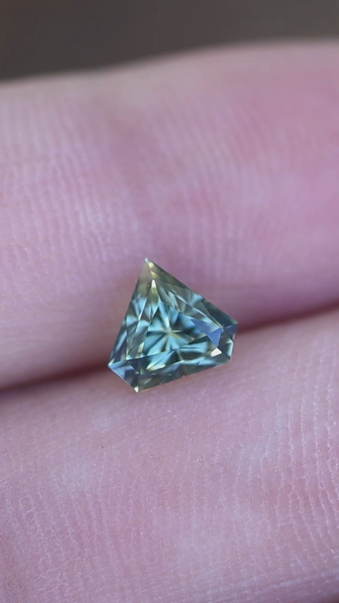 Rotating 1.06 carat parti blue green sapphire on hand displaying color shifts, brilliance, and modified shield cut from Madagascar.