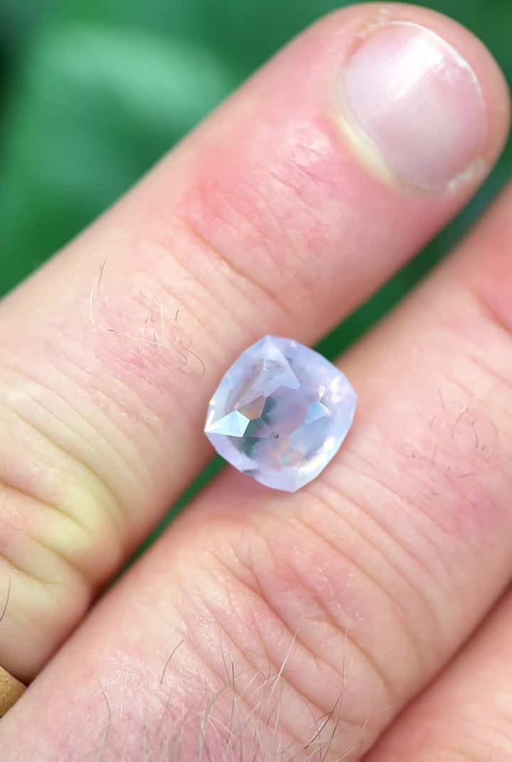 Opalescent light pink 5.12 carat Sri Lankan sapphire rotating on finger tips in natural lighting showing off dreamy coloring and precision faceting.