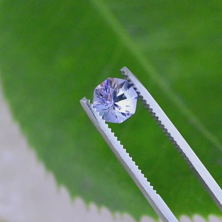 Close-up video of 2.38ct periwinkle violet Tanzanite octagon held in tweezers, precision cut gemstone from Tanzania displaying clarity, brilliance and vibrant violet blue tones