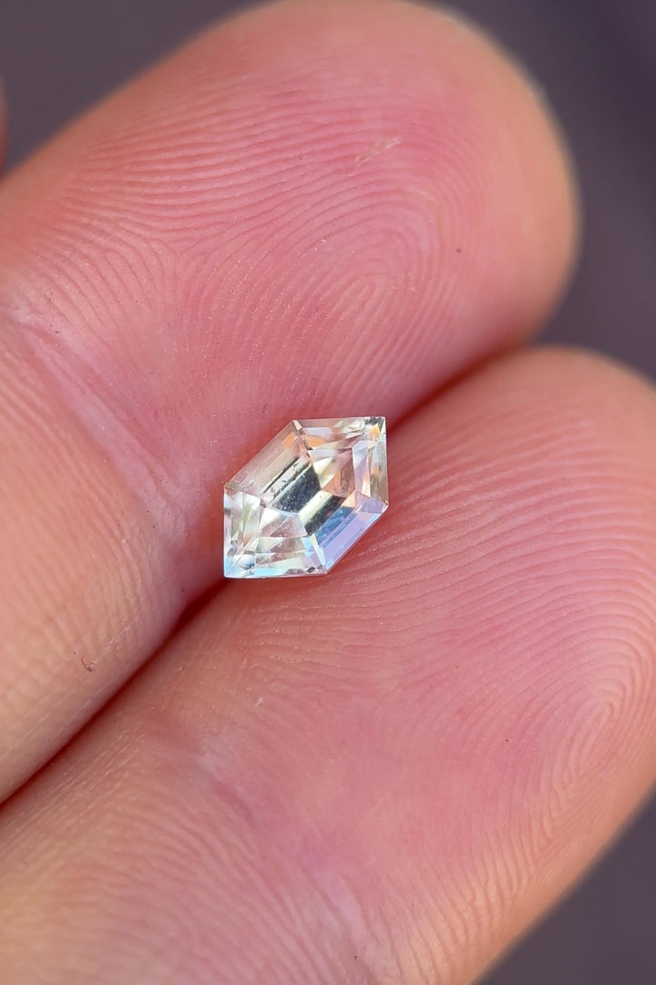 Hand-held pale yellow gray sapphire showing scale, soft color shift, and step cut reflections in natural light.