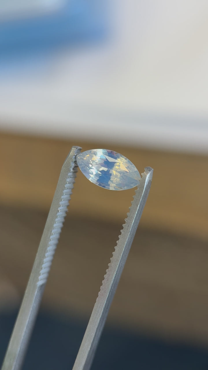 Macro video of 1.70CT opalescent powder blue sapphire rotating in tweezers, revealing its gentle shimmer and clarity in a precision marquise mixed cut, unheated sapphire from Ratnapura, Sri Lanka.